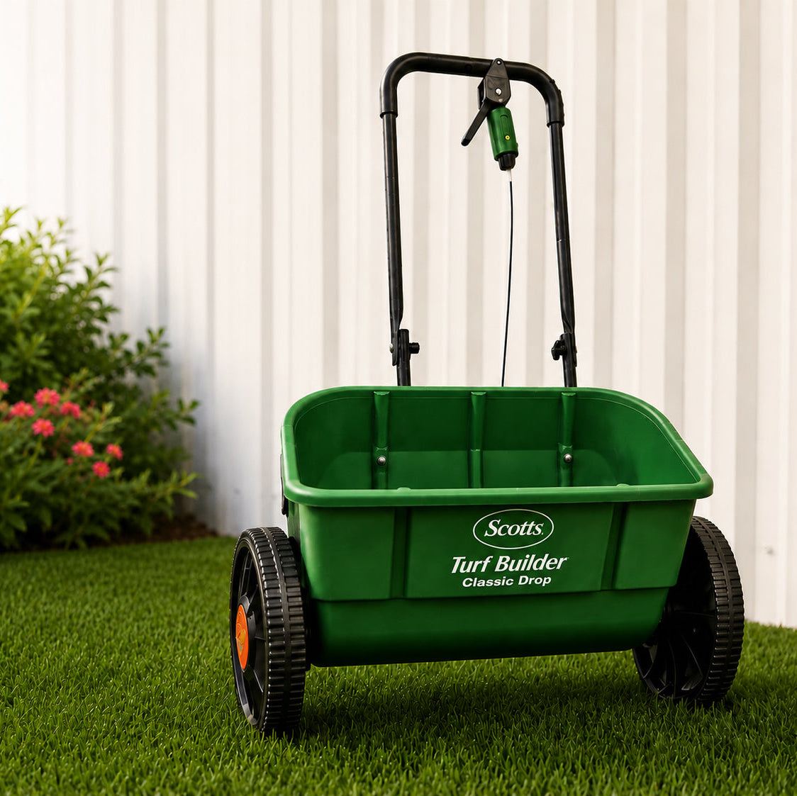 Green lawn spreader on grass with a white fence and plants in the background